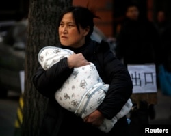 FILE - A mother carries her baby wrapped in a blanket in Beijing.
