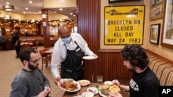 FILE - A waiter serves lunch at Junior's Restaurant in New York. NYC will soon require proof of COVID-19 vaccinations for anyone who wants to dine inside at a restaurant.