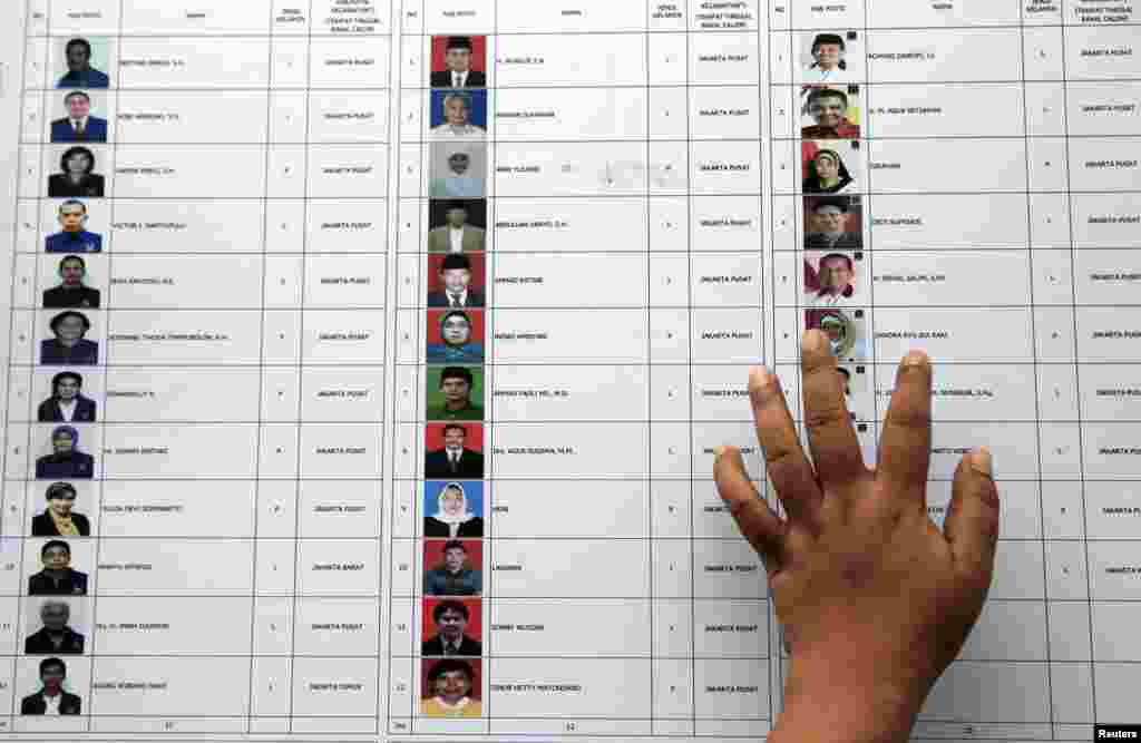 A person places a hand on a list of candidates for members of parliament at a polling station during voting for parliamentary elections in Jakarta, April 9, 2014.