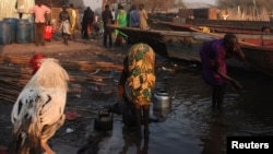 A women, right, displaced by the fighting in Bor county washes herself as another washes kettles, in the village of Mingkamen, in South Sudan, Jan. 14, 2014.