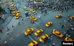 FILE - Yellow taxis pass people standing at Taksim Square, in Istanbul, Turkey, June 19, 2013.