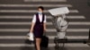 FILE - A CCTV security surveillance camera overlooks a street as a woman walks past following the spread of the novel coronavirus disease in Beijing, China, May 11, 2020. 