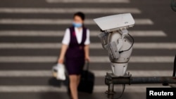 FILE - A CCTV security surveillance camera overlooks a street as a woman walks past following the spread of the novel coronavirus disease in Beijing, China, May 11, 2020. 