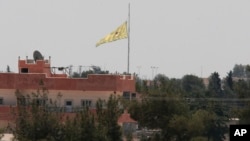 In this photo taken from the Turkish side of the border between Turkey and Syria, in Akcakale, southeastern Turkey, a flag of the Kurdish People's Protection Units, or YPG, flies over the town of Tal Abyad, Syria, June 16, 2015. 
