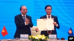 Vietnamese Prime Minister Nguyen Xuan Phuc, left, applauds as Minister of Trade Tran Tuan Anh, right, holds up a signed document during a virtual signing ceremony of the Regional Comprehensive Economic Partnership, or RCEP, trade agreement in Hanoi…
