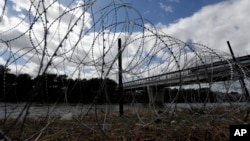 FILE - Razor wire recently placed by the U.S.military along the banks of the Rio Grande frames the McAllen-Hidalgo International Bridge at the U.S.-Mexico border, Nov. 3, 2018, in McAllen, Texas.
