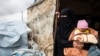 A Syrian woman carrying a baby looks out of a tent as she packs her belongings before leaving the Kurdish-run al-Hol camp holding relatives of alleged Islamic State group fighters, in the al-Hasakeh governorate in northeastern Syria, Nov. 16, 2020.