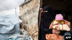 A Syrian woman carrying a baby looks out of a tent as she packs her belongings before leaving the Kurdish-run al-Hol camp holding relatives of alleged Islamic State group fighters, in the al-Hasakeh governorate in northeastern Syria, Nov. 16, 2020.