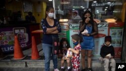 Ciudadanos con tapabocas se refugian de la lluvia en un comercio en Caracas, Venezuela.