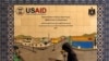 ARCHIVO - Un palestino camina junto a un cartel de cerámica de un proyecto de la Agencia de Estados Unidos para el Desarrollo Internacional (USAID) en Hebrón, en Cisjordania ocupada por Israel, el 31 de enero de 2019. 