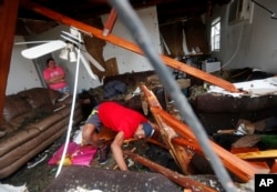 Dorian Carter looks under furniture for a missing cat after several trees fell on their home during Hurricane Michael in Panama City, Fla., Oct. 10, 2018.