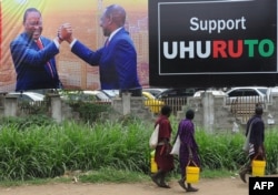 People walk past a campaign poster of Kenya's President Uhuru Kenyatta and Deputy President William Ruto, in Nairobi, Oct. 23, 2017, ahead of the repeat elections.
