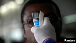 A health worker takes a passenger's temperature with an infrared digital laser thermometer at the Felix Houphouet Boigny international airport in Abidjan, Ivory Coast, Aug. 13, 2014. 
