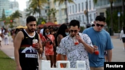 FILE - Young men read public safety precautions while enjoying the bars and restaurants on South Beach during spring break amid the coronavirus pandemic, in Miami, Florida, March 27, 2021. 