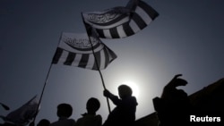 FILE - Supporters of the Jamaat-ud-Dawa Islamic organization are silhouetted against the sun as they raise their party flags while taking part in an anti-American rally in Lahore, May 25, 2012. 