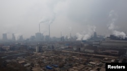 FILE - Smokestacks and cooling towers of a power plant rise above a low-rise neighborhood that borders a steel plant in Anyang, Henan province, China, Feb. 18, 2019.