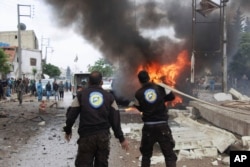 This photo provided by Azaz Media Office, a Syrian anti-government activist group, which has been authenticated based on its contents and other AP reporting, shows a Syrian White Helmet civil defense worker extinguishing a burning car at the explosion scene, in Azaz town, north Syria, Wednesday, May 3, 2017.