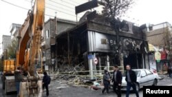 People walk near a burnt bank, after protests against increased fuel prices, in Tehran, November 20, 2019. 