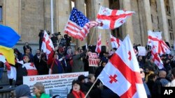 Demonstrators wave Georgian and American flags as they gather in Tbilisi, Georgia, Nov. 17, 2019. Hundreds of demonstrators gathered outside the parliament building to protest the failure of the legislature to pass promised election reform.