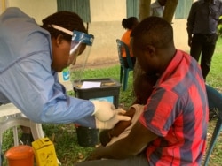 FILE - A father holds his 5-year-old daughter as she gets the Ebola trial vaccine in Kasese district Uganda, June 16, 2019. (H. Athumani for VOA)