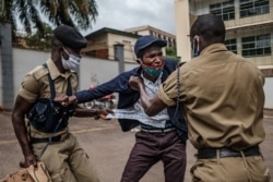 Ugandan police officers detain a demonstrator protesting for more food distribution by the government to people who have been struggling during the nationwide COVID-19 lockdown in Kampala, May 18, 2020.