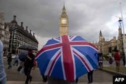 FILE - A pedestrian shelters from the rain beneath a Union Jack-themed umbrella near the Big Ben clock face and the Elizabeth Tower at the Houses of Parliament in central London, following the pro-Brexit result of the UK's EU referendum vote, June 25, 2016.