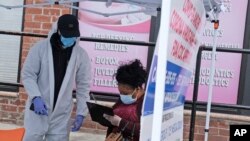 Penny Pierce fills out forms with the help of Taiwan McCall before getting tested for COVID-19 in the Harlem section of New York, April 20, 2020.