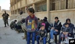 This photo released by the Syrian official news agency SANA, shows Syrian civilians, who fled fighting between the Syrian government forces and rebels, at an army checkpoint, in eastern Ghouta, a suburb of Damascus, Syria, March 13, 2018.