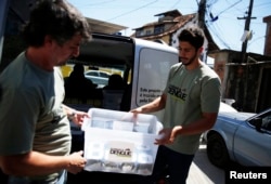 FILE - Technicians carry containers filled with Aedes aegypti mosquitoes with the dengue-blocking Wolbachia bacteria before they are released at the Tubiacanga neighborhood in Rio de Janeiro, Sept. 24, 2014. Similar work has been done in Australia, Vietnam and Indonesia.