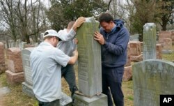 Workers hoist a headstone at the Chesed Shel Emeth Cemetery in University City, Mo., where over 150 headstones were tipped over. The cemetery is getting a show of support from volunteers, well-wishers and financial contributors from many faiths.