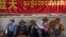 FILE - People rest in the shade beneath a government propaganda banner in Chinese and Tibetan near a neighborhood Tibetan Buddhist shrine in Lhasa, the capital of China's Tibet Autonomous Region, on June 3, 2021.