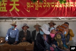 FILE - People rest in the shade beneath a government propaganda banner in Chinese and Tibetan in the Chengguan district of Lhasa in Tibet, western China, on June 3, 2021.