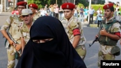 FILE - An Egyptian woman is seen in front of a group of soldiers as they stand guard during a protest near Cairo University.