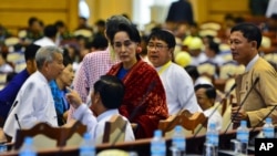 FILE - Leader of the National League for Democracy party (NLD) Aung San Suu Kyi, covered in a red-scarf stands among the lawmakers of the NLD ahead of a regular session of Myanmar's Lower House parliament in Naypyitaw, Myanmar. Although she is barred from taking the top post, the 70-year-old Aung San Suu Kyi insists she will still rule Myanmar through a figurehead candidate. 