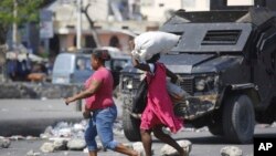 Pedestrians run past an armored police car in Port-au-Prince, Haiti, on March 7, 2024. Unrelenting gang attacks in Haiti have paralyzed the country and left it with dwindling supplies of basic goods.