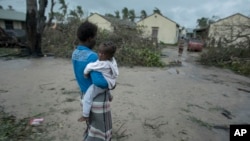 A woman and child near a school building being used as emergency shelter for some 300 local people who are unable to return to their homes following cyclone force winds and heavy rain in the coastal city of Beira, Mozambique, Sunday March 17, 2019.