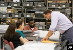 Employees at the Palm Beach County Supervisor of Elections office feed ballots through a machine as they count votes during a recount, Nov. 14, 2018, in West Palm Beach, Florida.