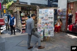 FILE - A man stops to read headlines, many featuring U.S. President Donald Trump's actions to jump-start construction on a promised border wall and his insistence that Mexico will foot the bill, in Mexico City, Jan. 26, 2017.