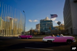FILE - Tourists ride in classic American convertible cars past the United States embassy, right, in Havana, Cuba, Jan. 12, 2017.