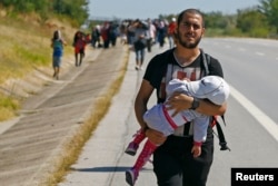 A Syrian migrant carries a baby as he walks towards the Greece border on a road near Edirne, Turkey, Sept. 15, 2015.