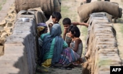 Indian women play with their children after finishing work at a brick factory on the eve of International Workers' Day at Chandrapur near Guwahati on March 7, 2016.