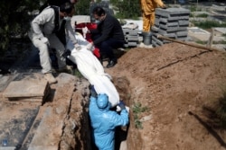FILE - Iranian men bury journalist Abdollah Zavieh, who died of COVID-19, at Behesht Zahra cemetery in Tehran, March 24, 2020.