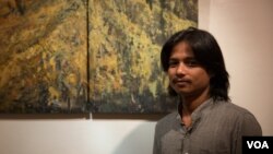 លោក នូវ ជានិច្ច ជាងគំនូរសហសម័យនៅទីក្រុងបាត់ដំបង ឈរថតរូបនៅខាងមុខរូបគំនូររបស់ខ្លួន នៅក្នុងការតាំងពិព័រណ៌ «មួយផ្នែកតូច» នៅហាងកាហ្វេទីនេះ ក្នុងទីក្រុងភ្នំពេញ ប្រទេសកម្ពុជា កាលពីថ្ងៃទី២៧ កញ្ញា ២០១៧។ (ទុំ ម្លិះ/VOA) 