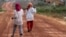 FILE - Women walk past houses, built for the residents being displaced by land sales, at Botum Sakor National Park in Koh Kong province, Feb. 20, 2012. About 200 families displaced by construction have returned to their homes, demanding more compensation.