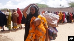 A woman, who fled amid a drought, carries her baby at a makeshift camp for displaced people on the outskirts of Mogadishu, Somalia on Tuesday, Sept. 26, 2023.