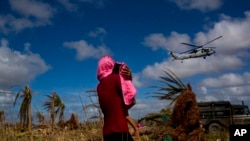 FILE - A Typhoon Haiyan survivor carries a child wrapped in a towel as he watches a helicopter landing to bring aid to the destroyed town of Guiuan, Samar Island, Philippines.