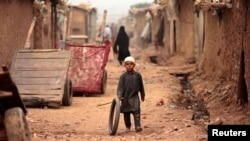 FILE - A boy plays with a tire on an a street in an Afghan refugee camp in Islamabad, Pakistan, Oct. 31, 2017. 