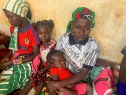 FILE - A woman who fled the violent rebellion in Central African Republic (CAR), sits with her family as they wait for their identification process in the border town of Garoua Boulai, Cameroon, Jan. 7, 2021.