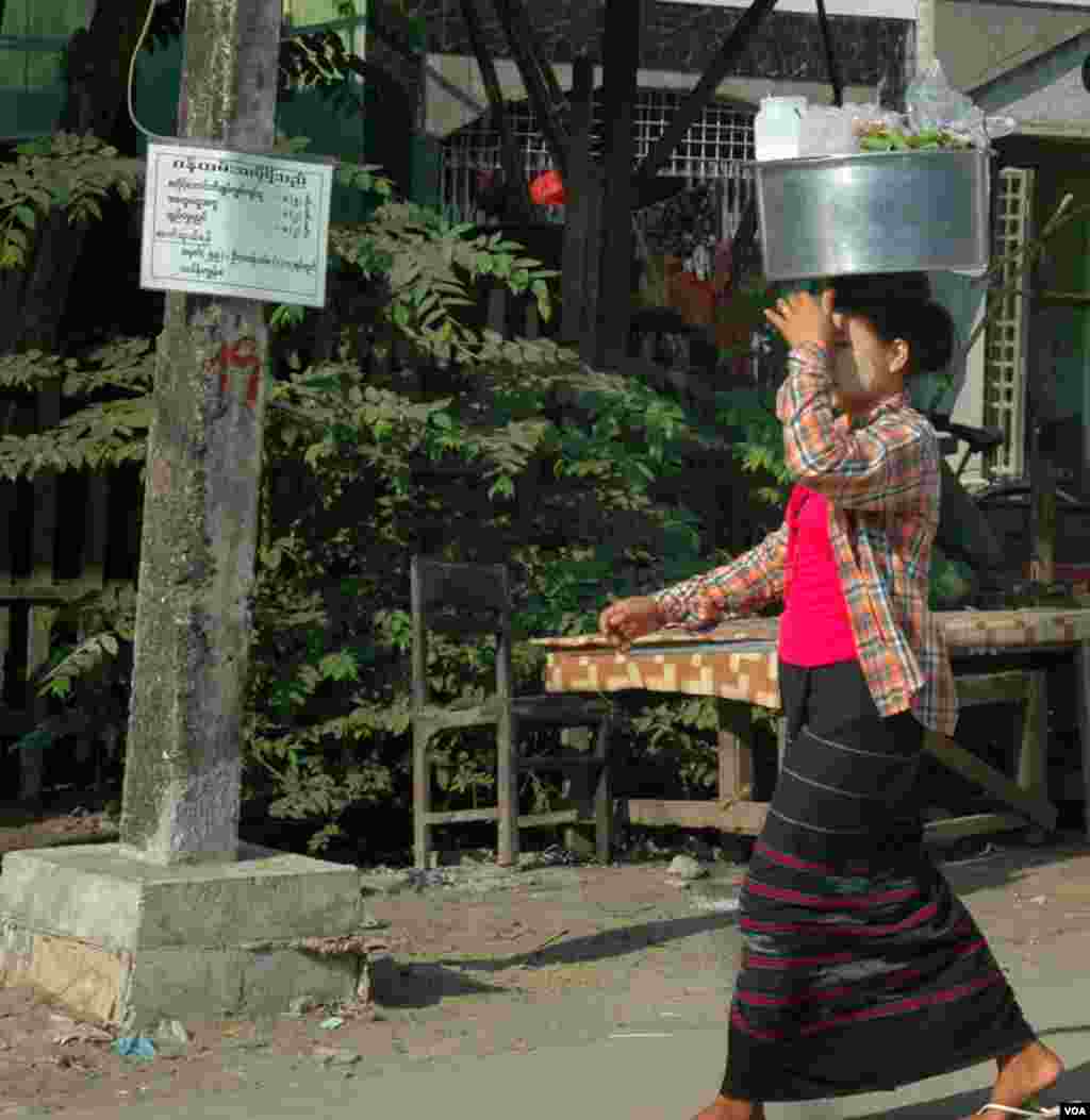 A longyi-clad woman with thanaka on her cheeks carrying food. (Steve Herman/VOA News)