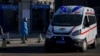 An ambulance passes a worker in protective gear outside a fever clinic in Beijing, Dec. 19, 2022.